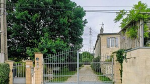 A gated entrance with a gravel path leading to a building with stone walls and a metal gate. - Near Bordeaux: air conditioning, parking, and a picturesque setting (Latresne)