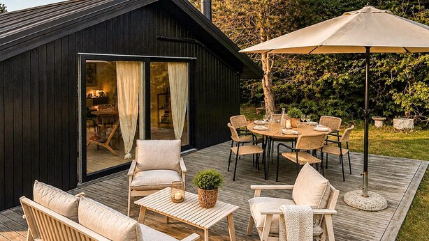 Une terrasse en bois avec des meubles d’extérieur, une table à manger pour quatre personnes et un grand parasol.