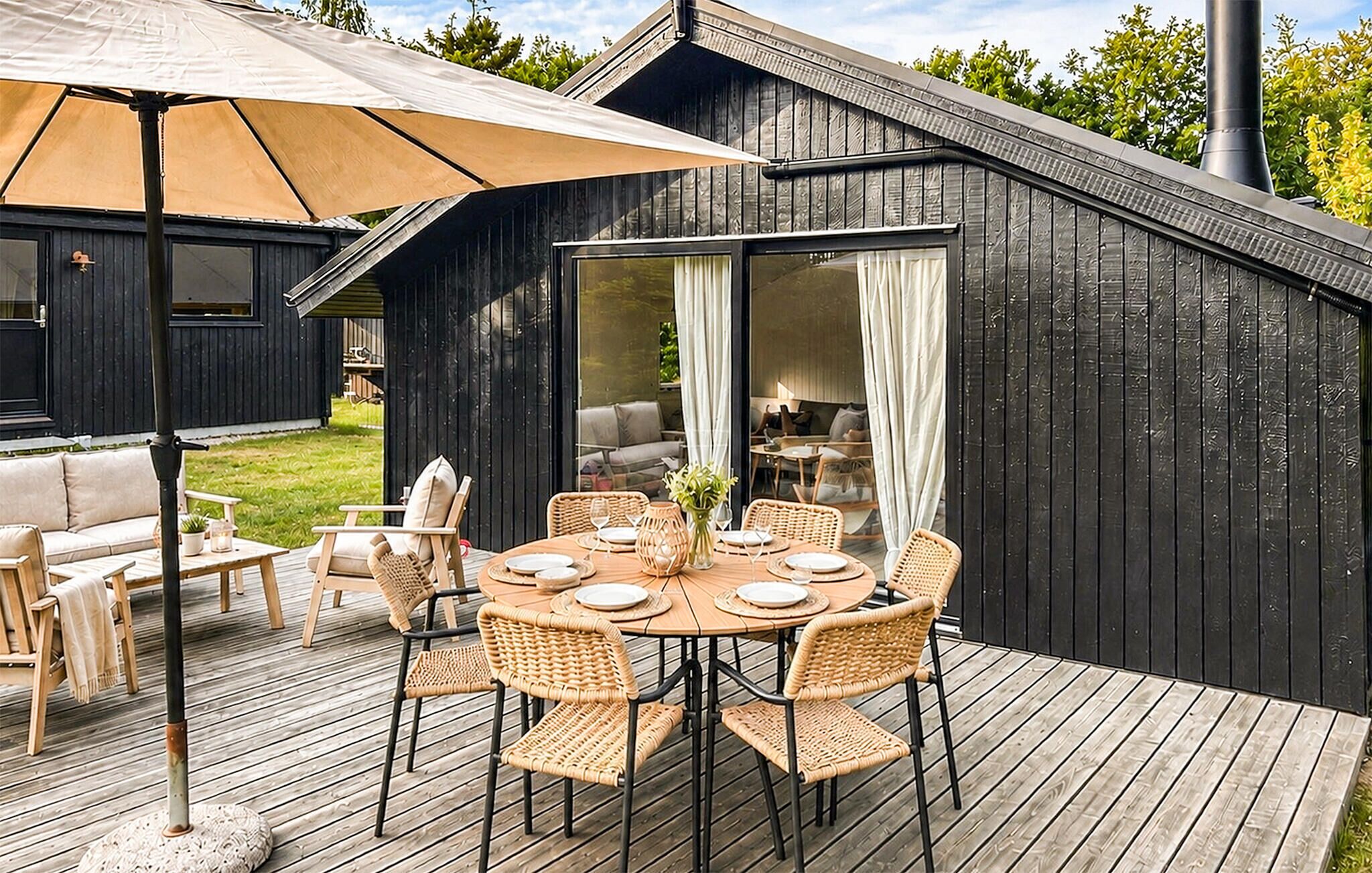 Eine Terrasse mit Esstisch, umgeben von Korbstühlen und einem Sonnenschirm.