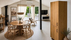 Un intérieur moderne avec une table de salle à manger ronde en bois, des chaises en osier, un grand meuble en bois et un téléviseur fixé au mur.