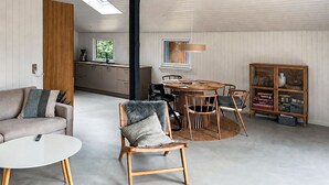 Un salon moderne comprenant un canapé, une table de salle à manger ronde avec des chaises, une bibliothèque et un coin cuisine avec une fenêtre.