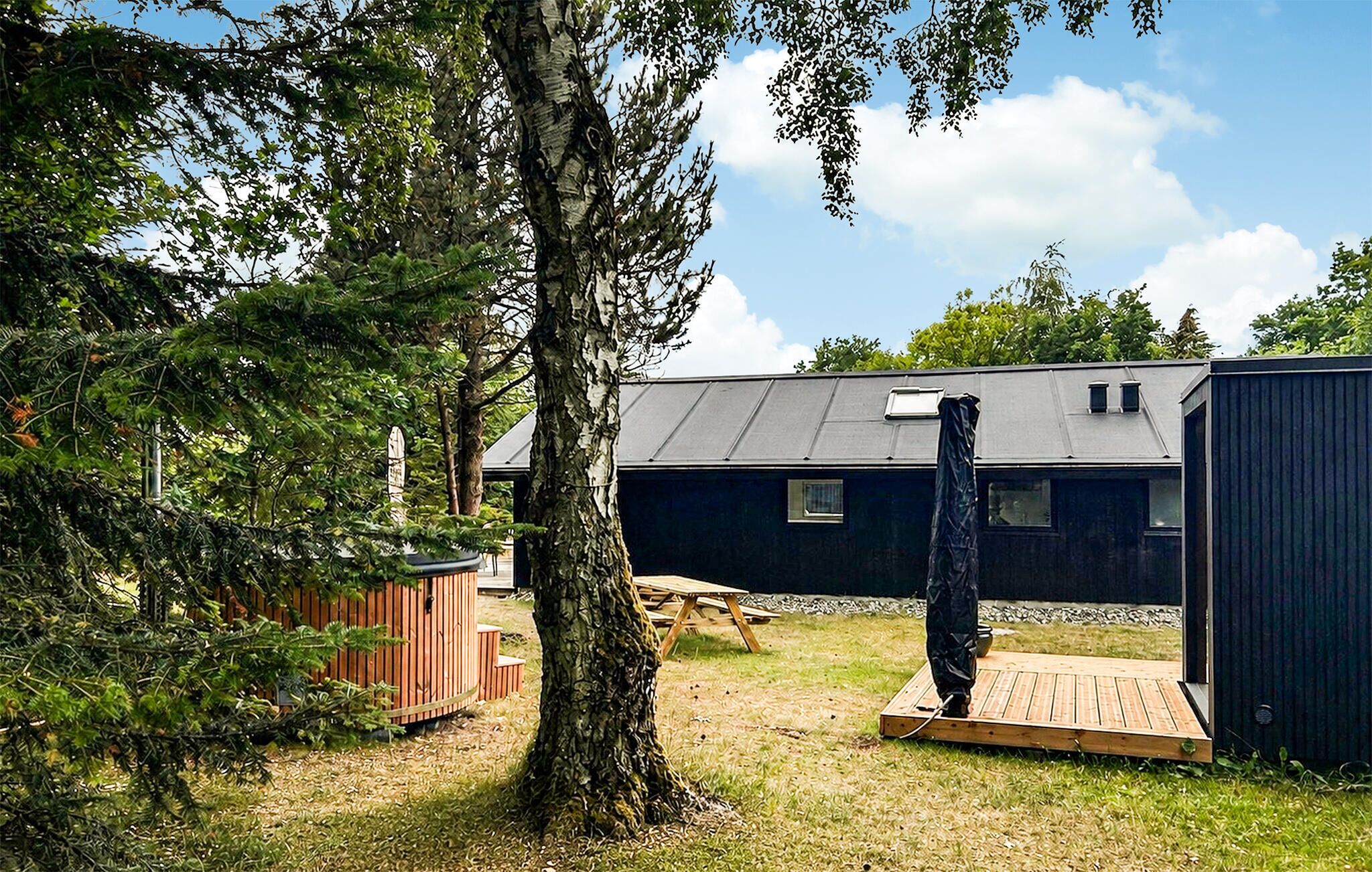 Ein kleines, dunkel gefärbtes Gebäude mit einem geneigten Dach, einer Holzterrasse und einem Baum im Vordergrund.