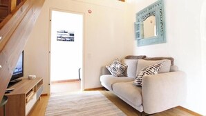 En stue med en sofa, et fjernsyn på et træstel og et mønstret tæppe.