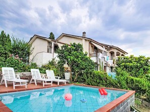 Une piscine entourée de chaises longues, avec un ballon rouge et un ballon bleu, le tout bordé de verdure et adossé à un immeuble doté de balcons.
