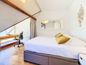 Een slaapkamer met een groot bed, een bureau met stoel, een raam en een spiegel aan de muur.