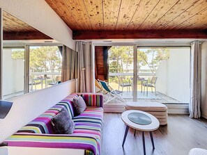 Ein modernes Interieur mit Holzboden, einem farbenfrohen, gestreiften Sofa, einem runden Tisch und Blick ins Freie.