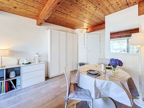 Een eethoek met een tafel voor twee personen, een wit kastje met lades en een houten plafond.