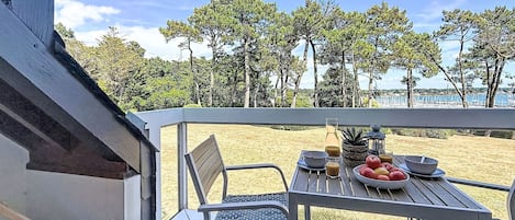 A terrace with a table set for dining, overlooking a beach and trees.