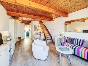 Un salón amplio con techo de madera, un sofá colorido a rayas, un sillón blanco y una pequeña mesa redonda.