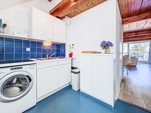 Una cocina moderna con lavadora, azulejos azules y vigas de madera en el techo.