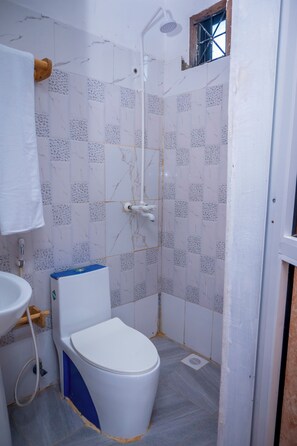 A bathroom with a toilet, sink, shower, and tiled walls. - Marumbi Beach House (Marumbi)