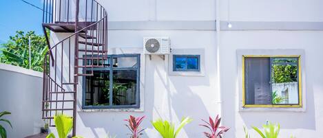 A two-story white building with a swimming pool, a spiral staircase, and potted plants.