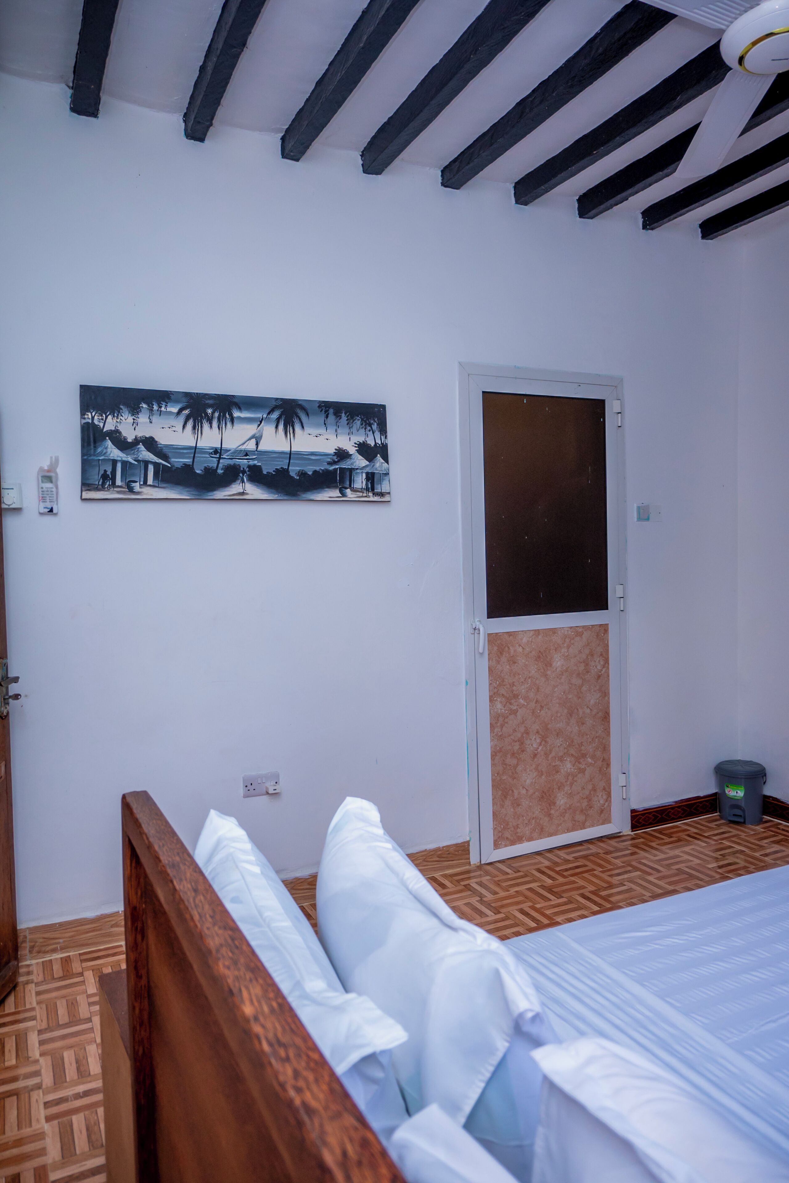 A bedroom with a bed, a door, a painting, and a ceiling fan.