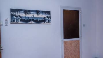 A bedroom with a bed, a door, a painting, and a ceiling fan.