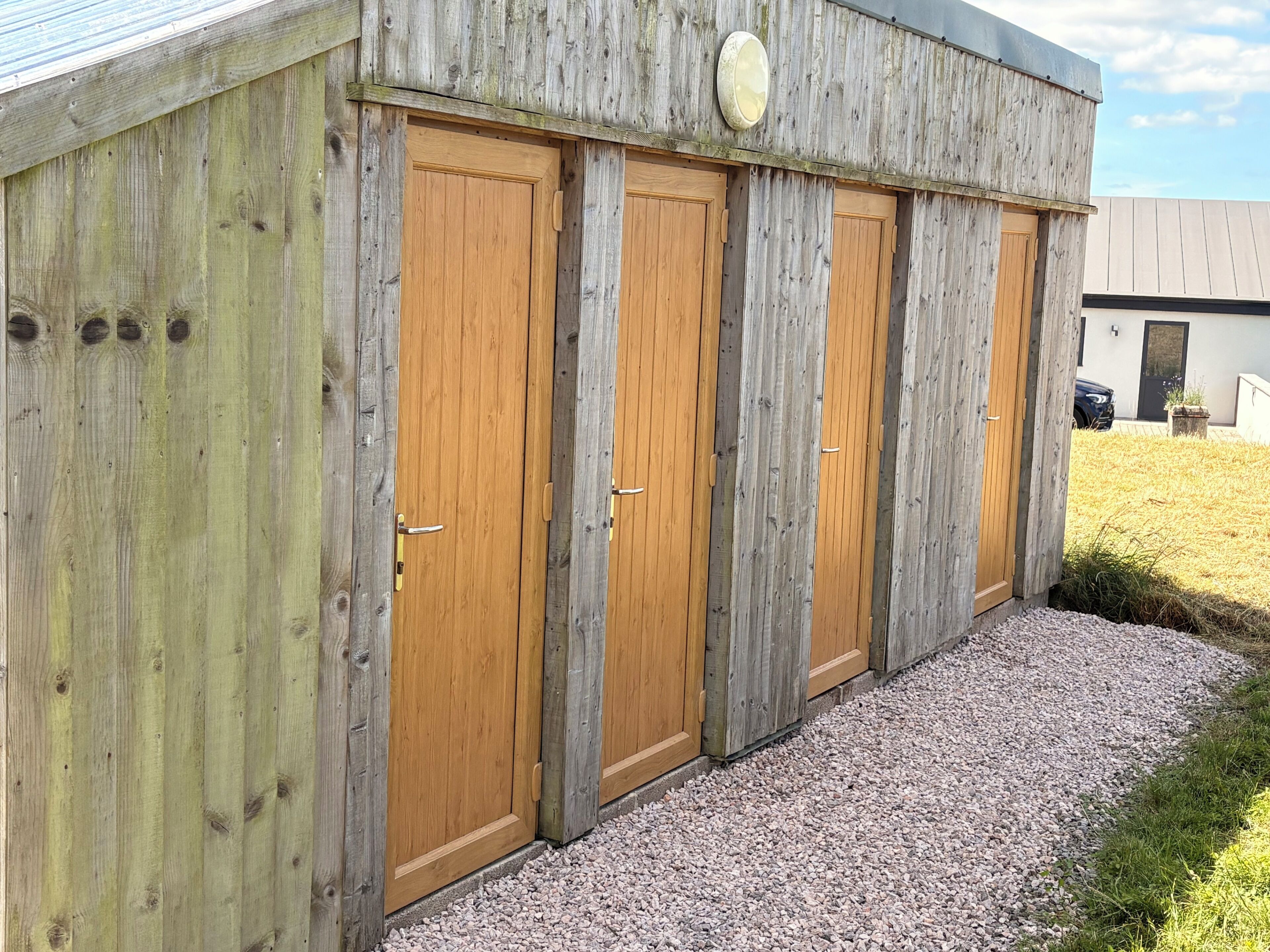 A wooden building with four doors, a gravel driveway, and a grassy area.