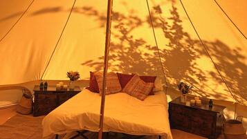 A tented accommodation with a bed, bedside tables, and a hanging light fixture.