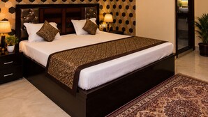 A hotel room with a large bed, a ceiling fan, an air conditioning unit, and a patterned wall.