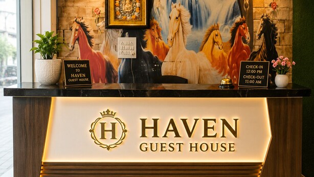 A hotel reception desk with a sign reading 'HAVEN GUEST HOUSE,' a framed picture of a horse, and a clock.