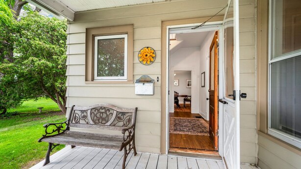 A wooden porch with a bench, a door leading inside, and a window with a decorative item above it. - Spacious 4BR/3BA home, blocks to downtown, parks, beach & farmers market. Fenced yard, pets welcome (Sturgeon Bay)