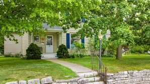 A two-story house with a stone wall, a front door, and a small front yard. - Spacious 4BR/3BA home, blocks to downtown, parks, beach & farmers market. Fenced yard, pets welcome (Sturgeon Bay)