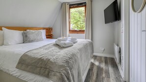 Ein Schlafzimmer mit einem Bett, einem Fernseher, einem Fenster mit Vorhängen und Holzboden.