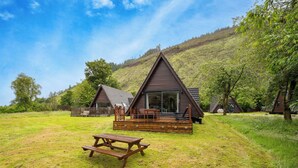 Eine Hütte mit einer Terrasse, einem Picknicktisch und einer Rasenfläche.