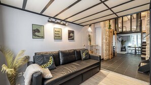 Ein modernes Wohnzimmer mit einem schwarzen Ledersofa, einem Essbereich mit Tisch und Stühlen sowie einer Treppe zu einer oberen Ebene.