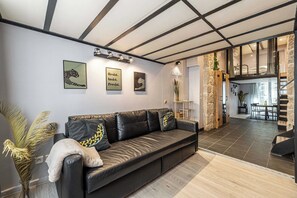 Ein modernes Wohnzimmer mit einem schwarzen Ledersofa, einem Essbereich mit Tisch und Stühlen sowie einer Treppe zu einer oberen Ebene.