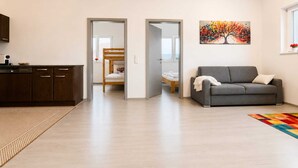A modern living room with a sofa, a painting, and a kitchen area with cabinets and a coffee machine. - Holiday idyll on Lake Wörthersee (Maria Saal)
