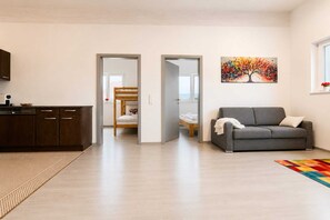 Una sala de estar moderna con un sofá, un cuadro y una zona de cocina con armarios y una máquina de café.