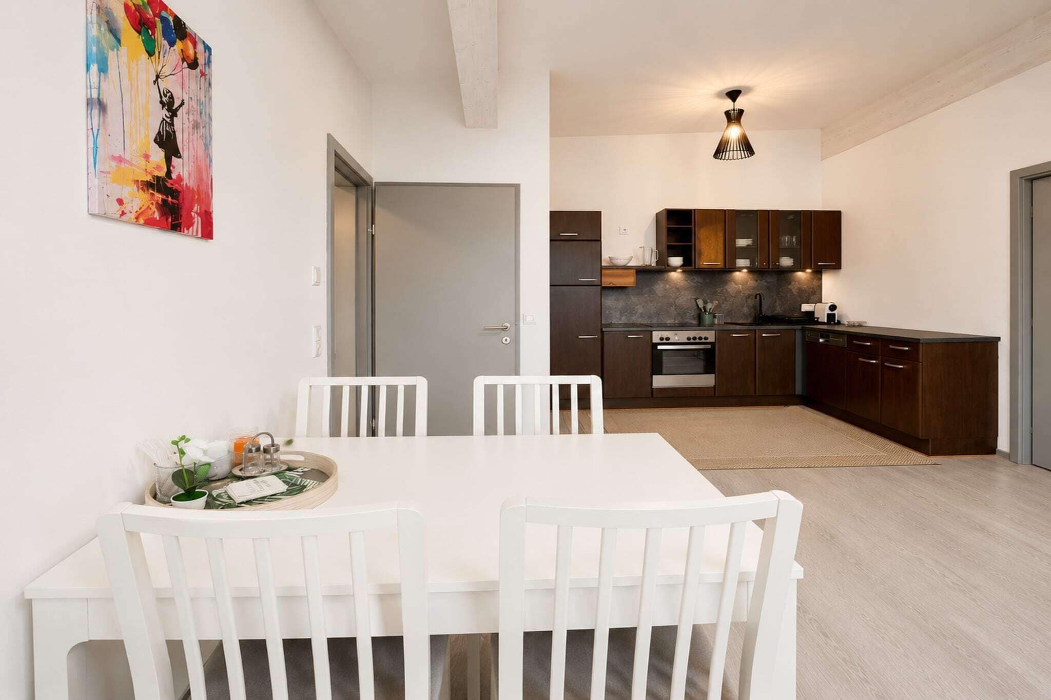 A modern kitchen with dark cabinets, a built-in oven, and a dining area with a white table and chairs.