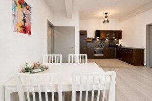 Una cocina moderna con gabinetes oscuros, horno empotrado y un comedor con mesa y sillas blancas.