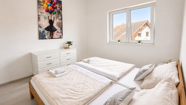 A bedroom with two beds, a dresser, a window with a view of a house, and a painting on the wall. - Holiday idyll on Lake Wörthersee (Maria Saal)