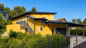 A modern yellow building with a covered outdoor area and a fenced garden. - Holiday idyll on Lake Wörthersee (Maria Saal)