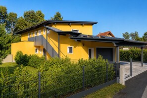 A modern yellow building with a covered outdoor area and a fenced garden.