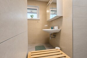 A small bathroom with a sink, mirror, window, and a small plant.