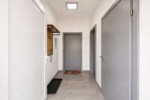Un pasillo estrecho con una puerta al final, un felpudo pequeño y un perchero en la pared izquierda.