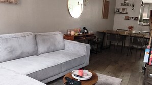 A living room with a grey sofa, a round coffee table with a tray, a dining area with a wooden table and chairs, and a large mirror on the wall. - The cozy little house in Theux, near Spa, the F1 circuit, and other attractions (Theux)