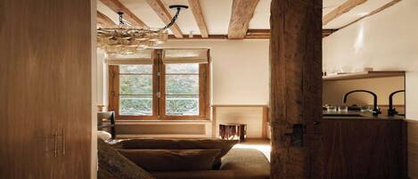 A rustic room with a wooden ceiling, a large window, a sofa, and a kitchen area.