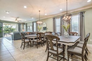 A dining area with a large wooden table and chairs, a ceiling fan, and pendant lights. - Arcade Games Room + Private Pool | Mins to Disney | Cosmic Clubhouse (Kissimmee)