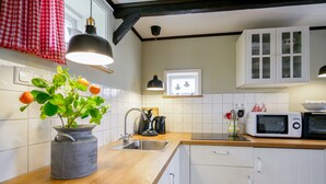 Una cucina con piano di lavoro in legno, lavello, una pianta in vaso, bollitore, forno a microonde e mobili bianchi.
