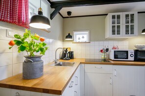 Eine Küche mit Holzarbeitsplatte, Spüle, einem Blumentopf, Wasserkocher, Mikrowelle und weißen Schränken.