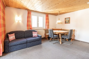 Ein gemütliches Zimmer mit einer Couch, Esstisch, Stühlen, einem Heizkörper und einem Fenster mit Vorhängen.