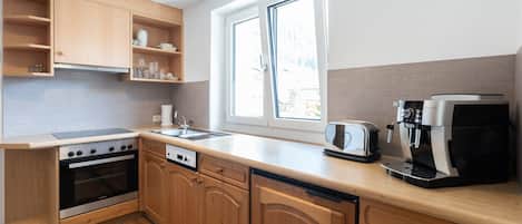 A modern kitchen with wooden cabinets, a built-in oven, a coffee machine, and a window providing natural light.