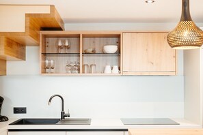 A kitchen with a black sink, wooden shelves above, and a pendant light. - Relax Suite with Jacuzzi (Burg Reuland)