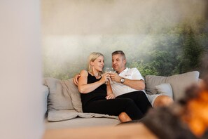 A couple sitting on a sofa with a blurred natural background. - Relax Suite with Jacuzzi (Burg Reuland)