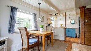 A dining area with a wooden table and chairs, a kitchen in the background, and a view of the outdoors. - Holiday home in Callantsoog near beach (Callantsoog)