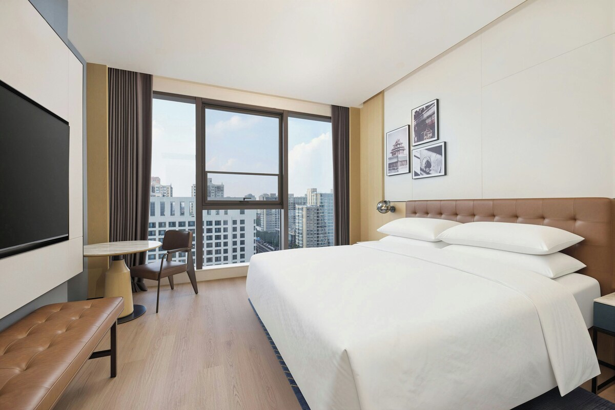 A hotel room with a large bed, a desk, a chair, and a TV.