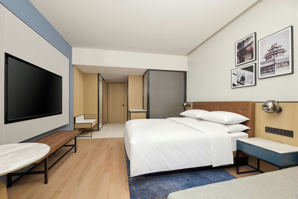 A modern hotel room with a large bed, a flat-screen TV, a desk, and a seating area.