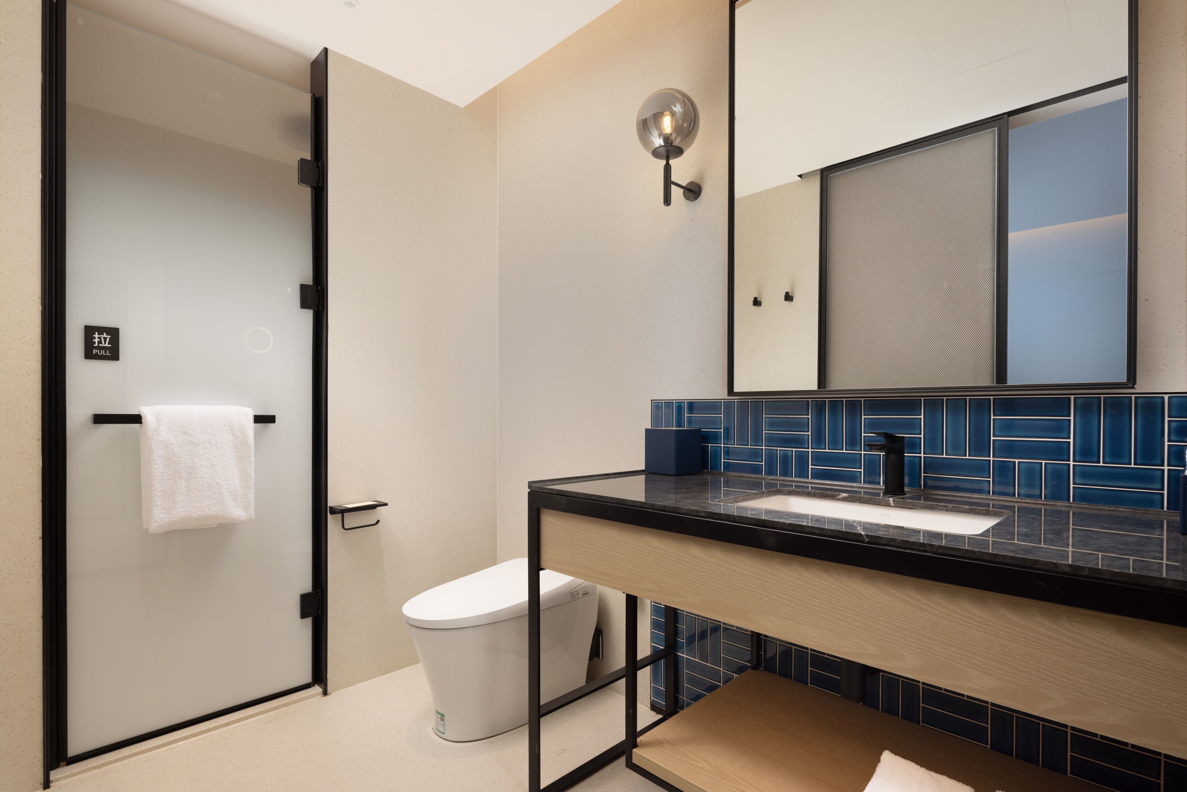 A modern bathroom with a glass shower door, a white toilet, a sink with a black countertop, and a mirror above the sink.